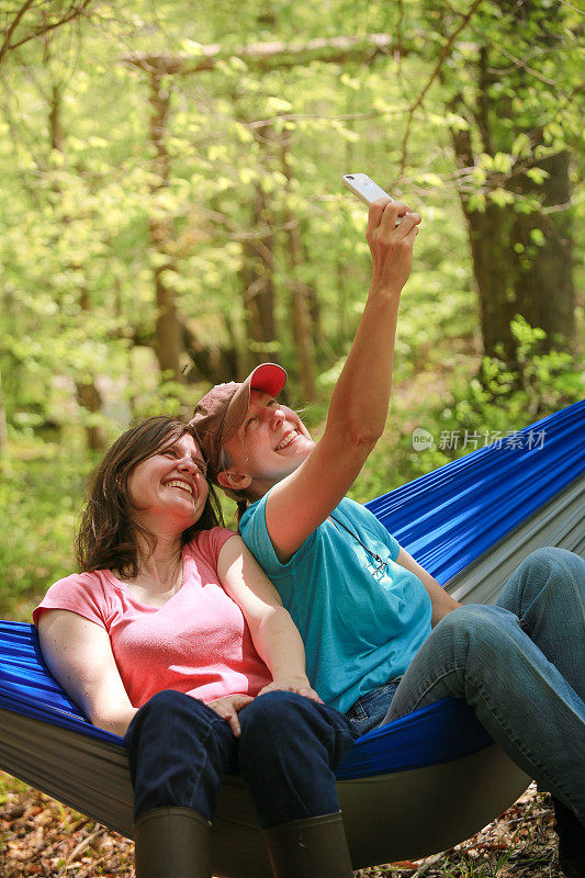 Two Women Friends Sitting in Camping Hammock Taking Selfies on Phone